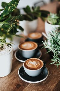 A row of 3 cups of coffee with foam designs